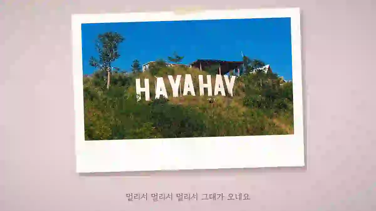 분홍 바탕 가운데 언덕 위 큰 글자 간판이 보이는 가로 풍경 사진이 폴라로이드 한 장으로 놓인 장면