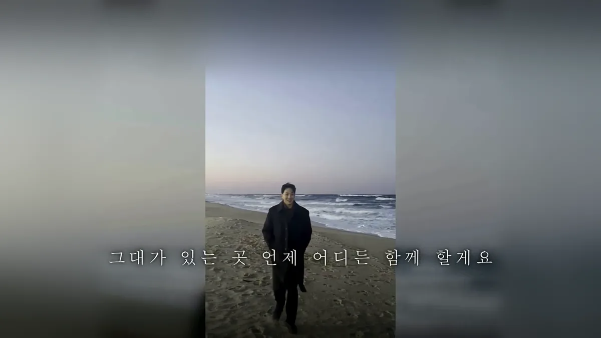 흐린 바닷가를 걸어오는 신랑의 세로 영상이 화면 가운데에 놓이고, 그 아래 가사 자막 한 줄이 뜬 축가 영상 장면