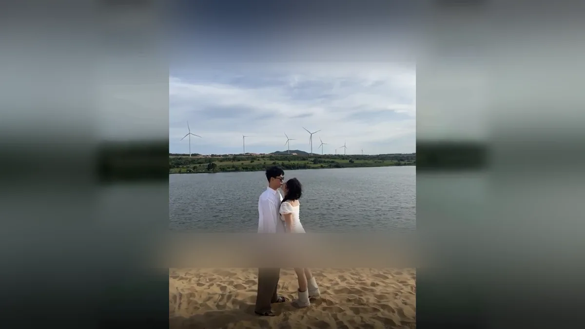 풍력발전기가 보이는 호숫가 모래밭에서 두 사람이 마주 선 세로 영상을 가로 화면 가운데에 놓은 장면